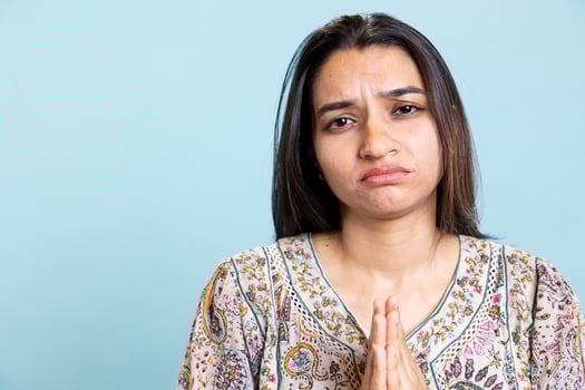 Religious indian girl praying to god and showing optimism on camera, talking to jesus with respect and devotion against blue background. Christian faithful woman expresses her belief, worship. photo