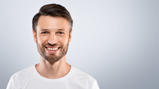 Handsome young bearded man smiling at camera over grey studio background. Attractive cheerful man posing for male magazine or blog, youth, healthy lifestyle and male cosmetology concept photo