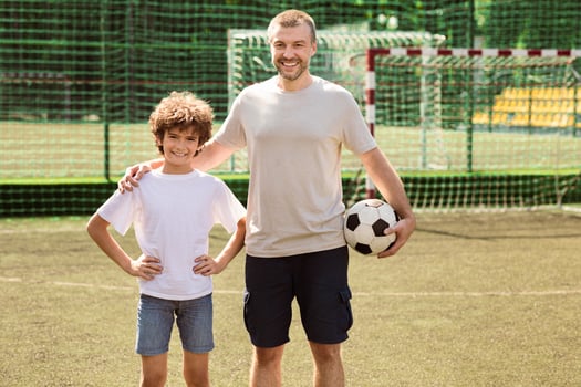 Sports Concept. Portrait of smiling man holding soccer ball and standing with boy on playground, posing at camera photo