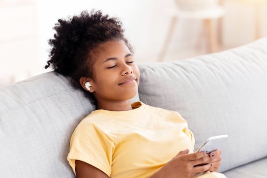 Listen Music Online. African American Teen Girl Enjoying Song Wearing Earbuds Lying On Sofa Relaxing At Home. photo