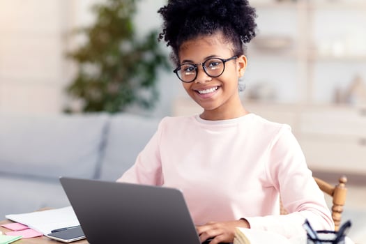 Black Teen Girl At Laptop Learning Online Smiling To Camera Sitting At Table At Home, Wearing Eyeglasses. Distant School Education photo
