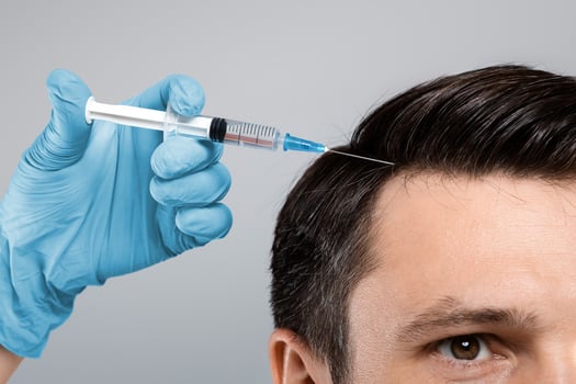 Mesotherapy for hair. Closeup of young man getting injections in head, grey panorama background. Millennial man having mesotherapy session at beauty salon, therapist in protective glove with syringe photo