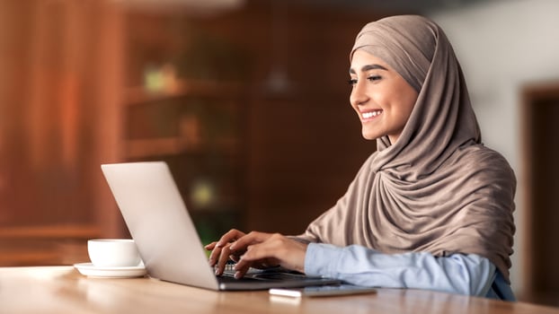 Happy arab woman freelancer chatting with clients on laptop, sitting at cafe, empty space photo