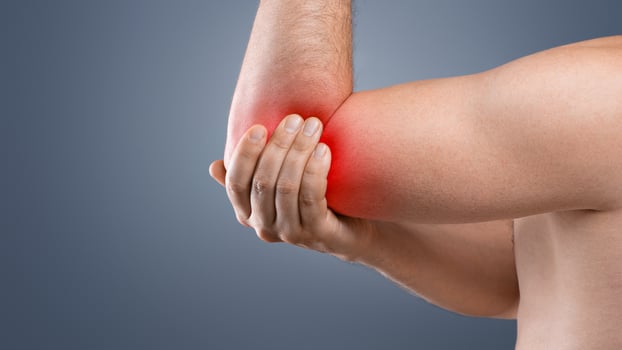 Cropped of topless man having pain in his elbow, touching his injured hand highlighted with red, side view, copy space. Closeup of unrecognizable guy rubbing sore elbow, grey studio background photo