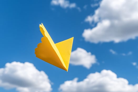 A yellow paper airplane flying in the sky photo
