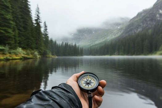 A person holding a compass in front of a lake photo