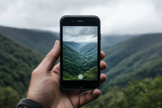 A person holding an iphone in front of a mountain landscape photo