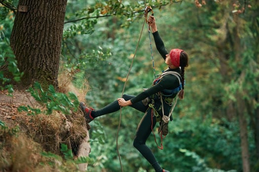 View from, the side, hanging on the rope. Woman is doing climbing in the forest by the use of safety equipment photo