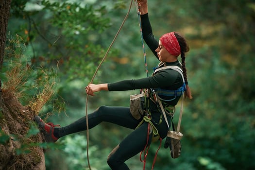 In sportive ,clothes, high up on the rope. Woman is doing climbing in the forest by the use of safety equipment photo