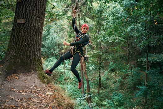 Looking, to the side, hanging on the rope. Woman is doing climbing in the forest by the use of safety equipment photo