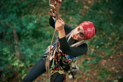 Focused, on, the climbing ,up. Woman is in the forest, using the safety equipment photo