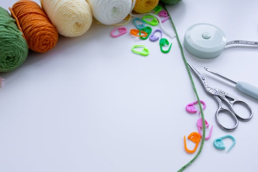 Colorful yarn balls with crochet tools and stitch markers on white surface photo