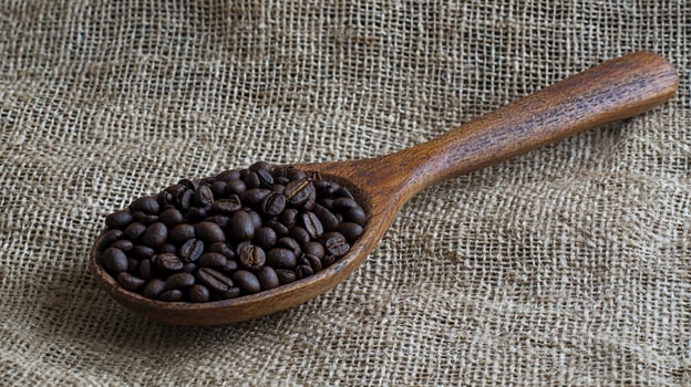 Close-up shot of coffee beans inside a wooden spoon, on a burlap background. photo
