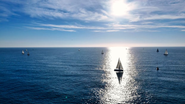 Sailboats glide gracefully across the shimmering blue ocean under a radiant sky at sunset photo
