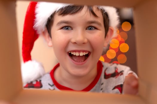A happy, boy in a New Year's jumper and a Santa Claus hat smashes into a box photo