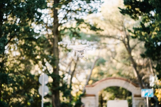 White drone flies through the park near the brick gate photo