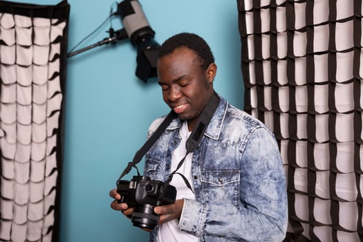 Professional male photographer holding camera and reviewing his pictures during a photoshoot session in studio. Young black cameraman standing and happily looking at images on his dslr screen. photo