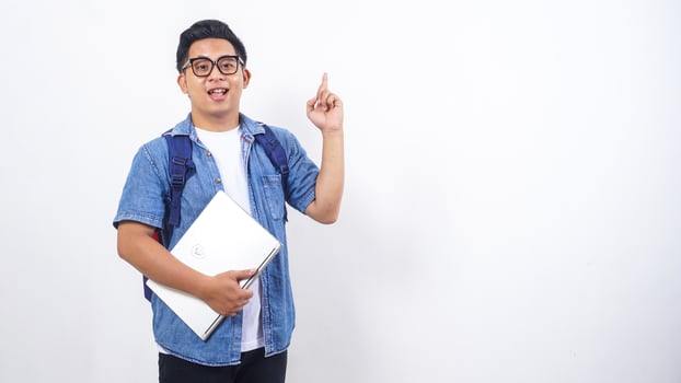 Portrait of handsome young Asian male university student in casual outfit with backpack and laptop isolated on white background with copy space photo