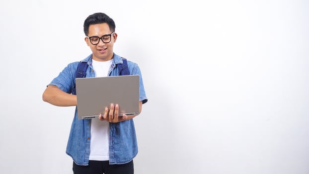Portrait of handsome young Asian male university student in casual outfit with backpack and open laptop isolated on white background photo