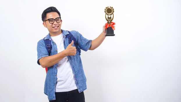 Portrait of happy young Asian male university student in casual outfit with backpack is holding trophy isolated on white background photo