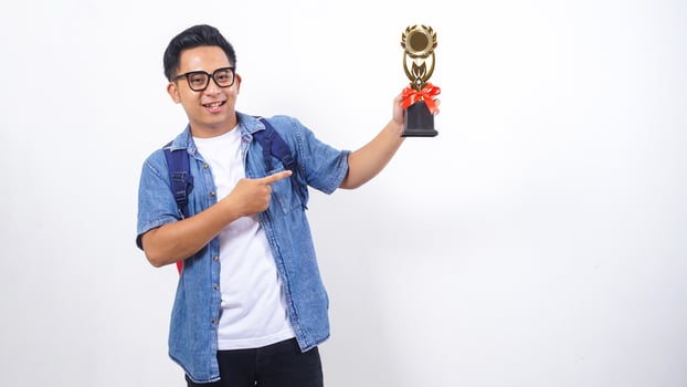 Portrait of handsome young Asian male university student in casual outfit with backpack is holding trophy isolated on white background photo