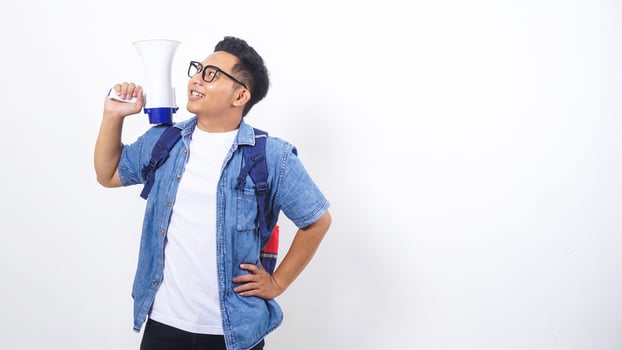 Close up of happy young Asian male university student in casual outfit with backpack is holding megaphone isolated on white background photo