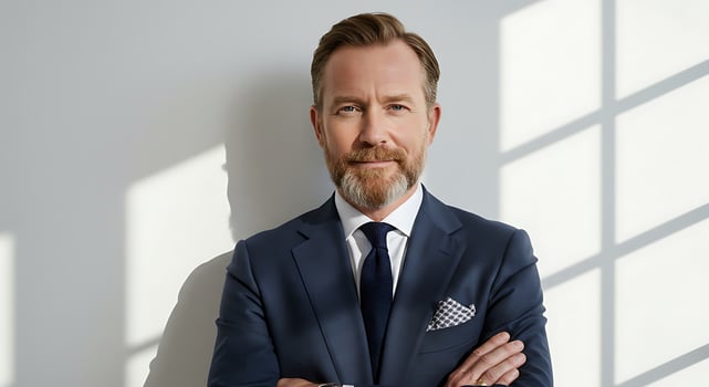 A man with a beard and a suit is standing in front of a window photo