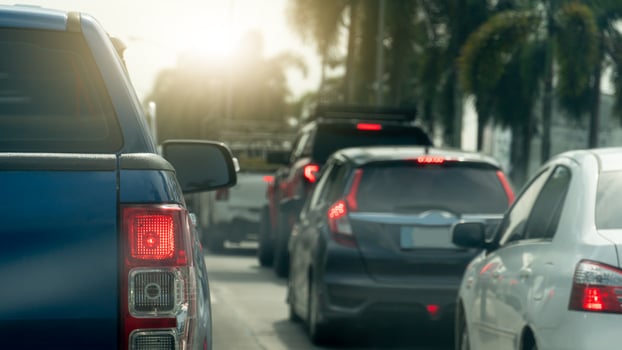Rear side of blue pickup car with turn on brake light. Many car queue up due to traffic congestion. Side road with trees. Background of bright light of the sun shines. photo