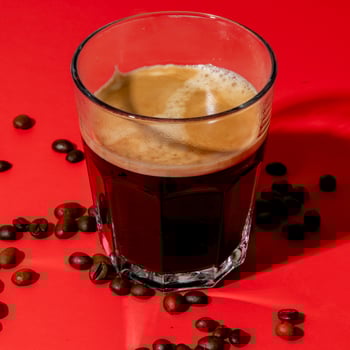 Fresh espresso in a glass with scattered coffee beans on red background, perfect for morning energy boost or International Coffee Day photo