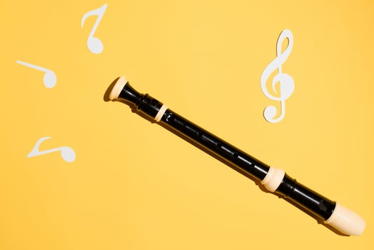 Flute, notes and treble clef, flat lay on a yellow background. Musical classical instrument photo