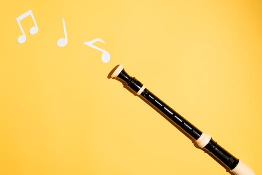 Musical black flute and notes cut from paper on a yellow background. Flat lay. photo