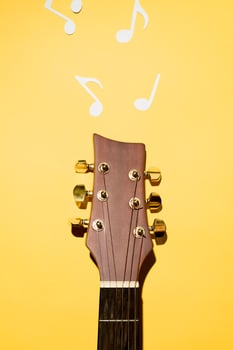 Acoustic guitar neck and sheet music cut from paper. Yellow background, flat lay. photo