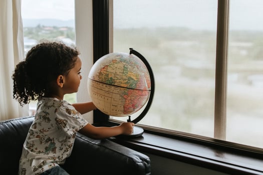 A young girl looking at a globe on a window sill photo