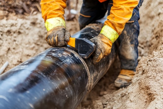 A man in an orange shirt and yellow gloves is working on a pipe photo