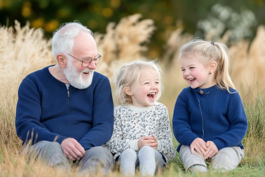 An older man and two young girls laughing in a field photo