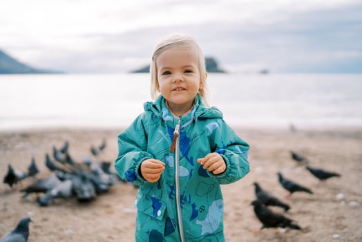 Little smiling girl stands on the beach near a flock of pigeons photo