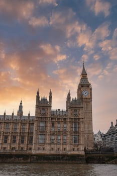 Elizabeth Tower, part of the Palace of Westminster, stands against a sunset sky with orange and pink hues. The River Thames reflects the soft evening light. photo