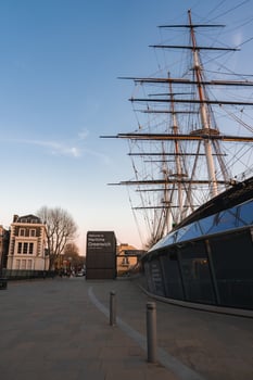The Cutty Sark's tall masts and rigging stand above a modern glass base in Greenwich, London, with a Maritime Greenwich sign and nearby trees. photo