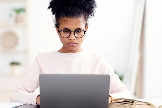 E-Learning. Concentrated Black Teen Girl At Laptop Learning Doing Homework Online Sitting At Desk At Home photo