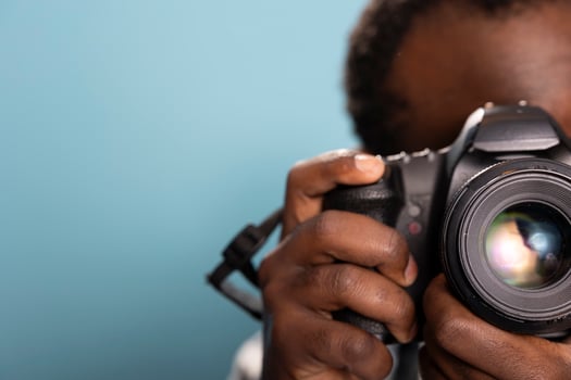 Closeup of black male photographer using a professional camera in a studio with a blue background. Selective focus on an african american man holding and demonstrating how to use a DSLR. photo