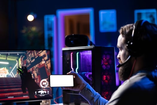 Man watching tutorial on isolated screen mobile hone while playing first person shooter videogame with guns. Gamer learning to play game by looking at online guide on mockup cellphone photo
