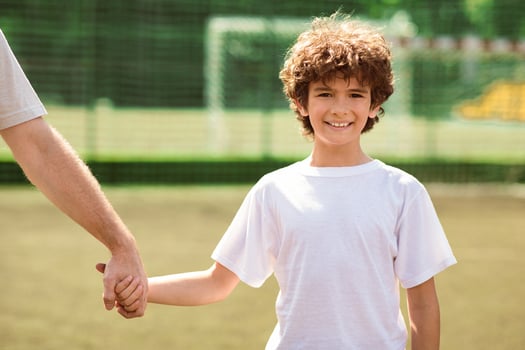 Support Concept. Portrait of smiling curly boy holding male hand and looking at camera, standing on football field photo