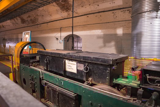Indoor display of a green and black locomotive labeled 'Cell Explosion' in a brick walled underground space with arched doorways and visible piping. photo