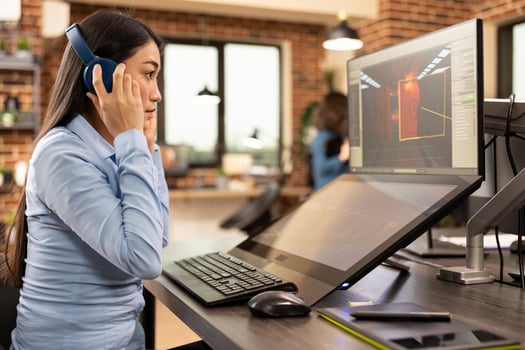 Female designer puts on her headphones and works on digital monitors, improving visual designs in a modern studio. Asian woman touching her earphones, and looking at her designs on computer screen. photo