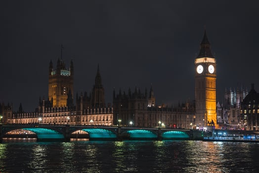 Big Ben and the Houses of Parliament glow against the night sky. Westminster Bridge spans the River Thames, with turquoise lights reflecting on the water. photo