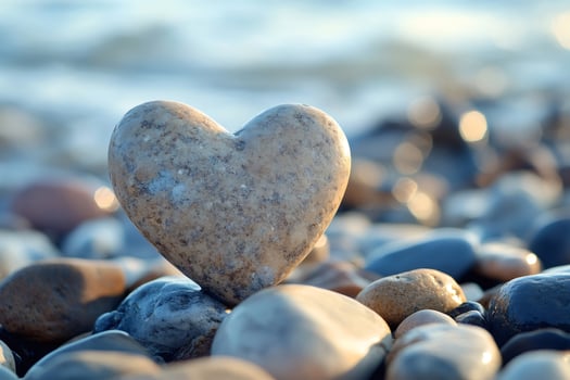 Heart shaped stone balancing on rocks by the sea at sunset photo