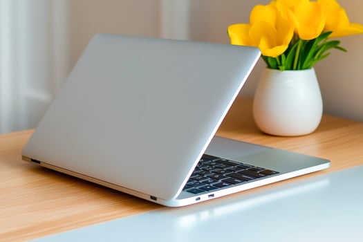 Modern silver laptop showing keyboard and trackpad with yellow flowers on desk photo