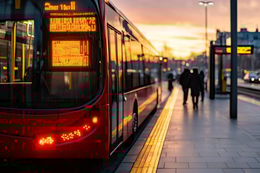Red bus waiting at station during golden hour sunset with passengers walking by photo
