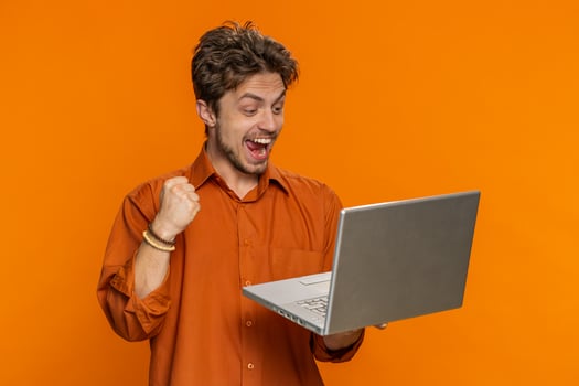 Excited happy young man working on laptop winning online lottery game celebrating success victory photo
