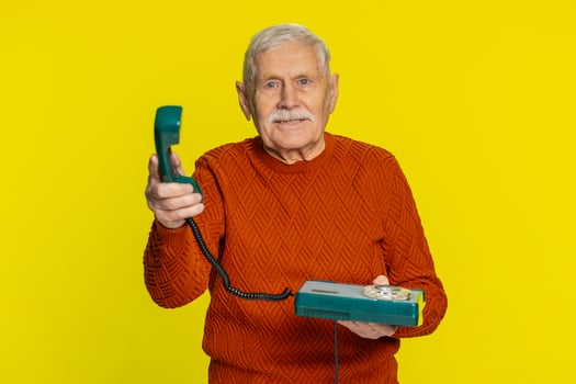 Senior man talking on wired landline vintage telephone, advertising proposition of conversation photo